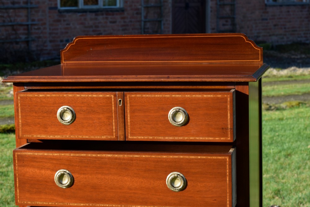 An Edwardian mahogany tall chest of drawers featuring fine string inlay, brass ring handles, five drawers, a low raised backboard, and square tapered legs. View XIII