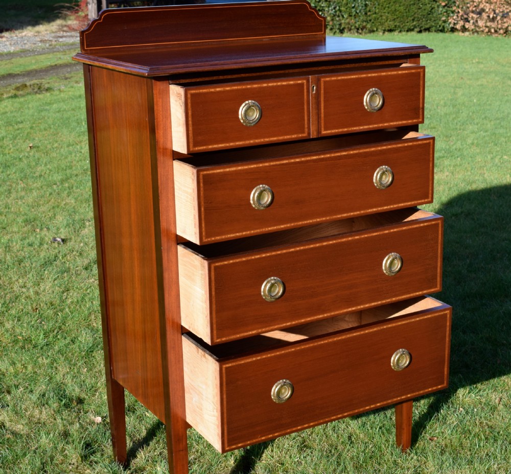 An Edwardian mahogany tall chest of drawers featuring fine string inlay, brass ring handles, five drawers, a low raised backboard, and square tapered legs. View XVI