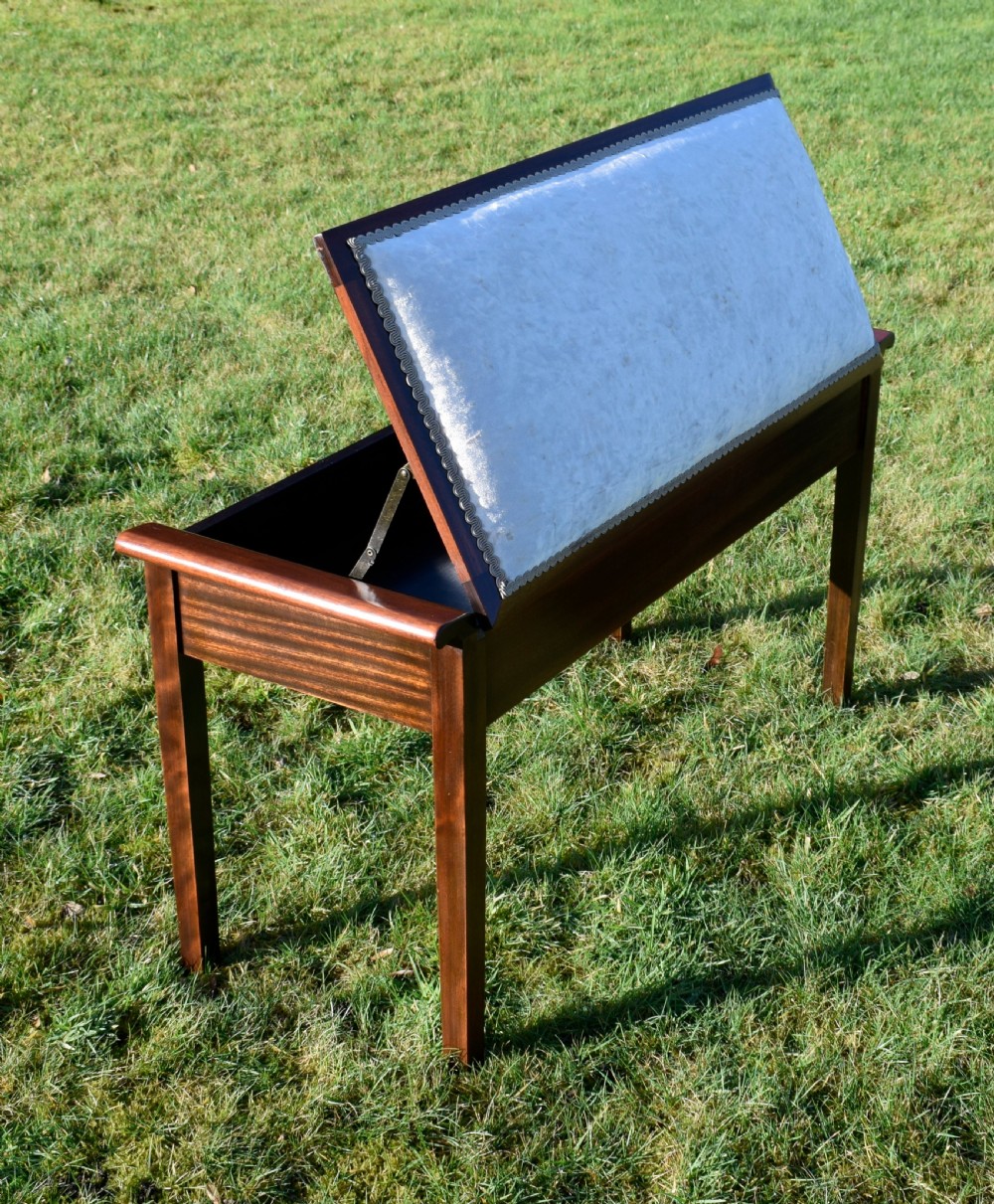An Art Deco dark mahogany duet piano stool featuring a cushioned pale pink velvet seat with braided gimp trim and straight tapered legs. View II