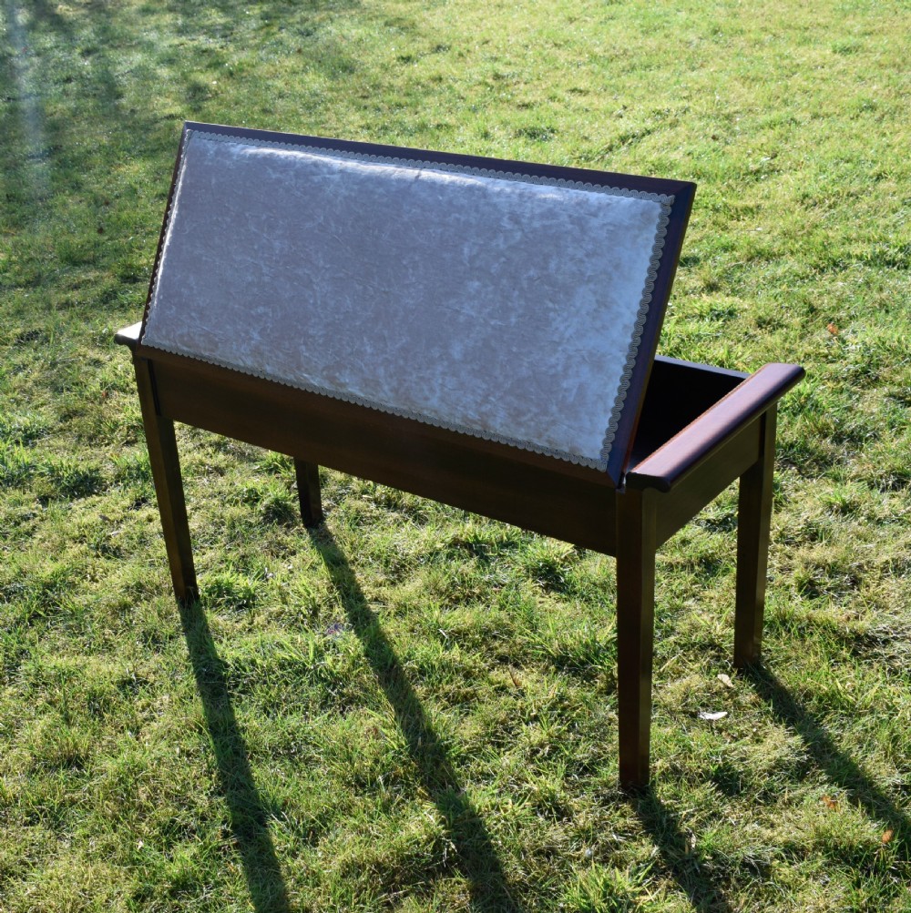 An Art Deco dark mahogany duet piano stool featuring a cushioned pale pink velvet seat with braided gimp trim and straight tapered legs. View III