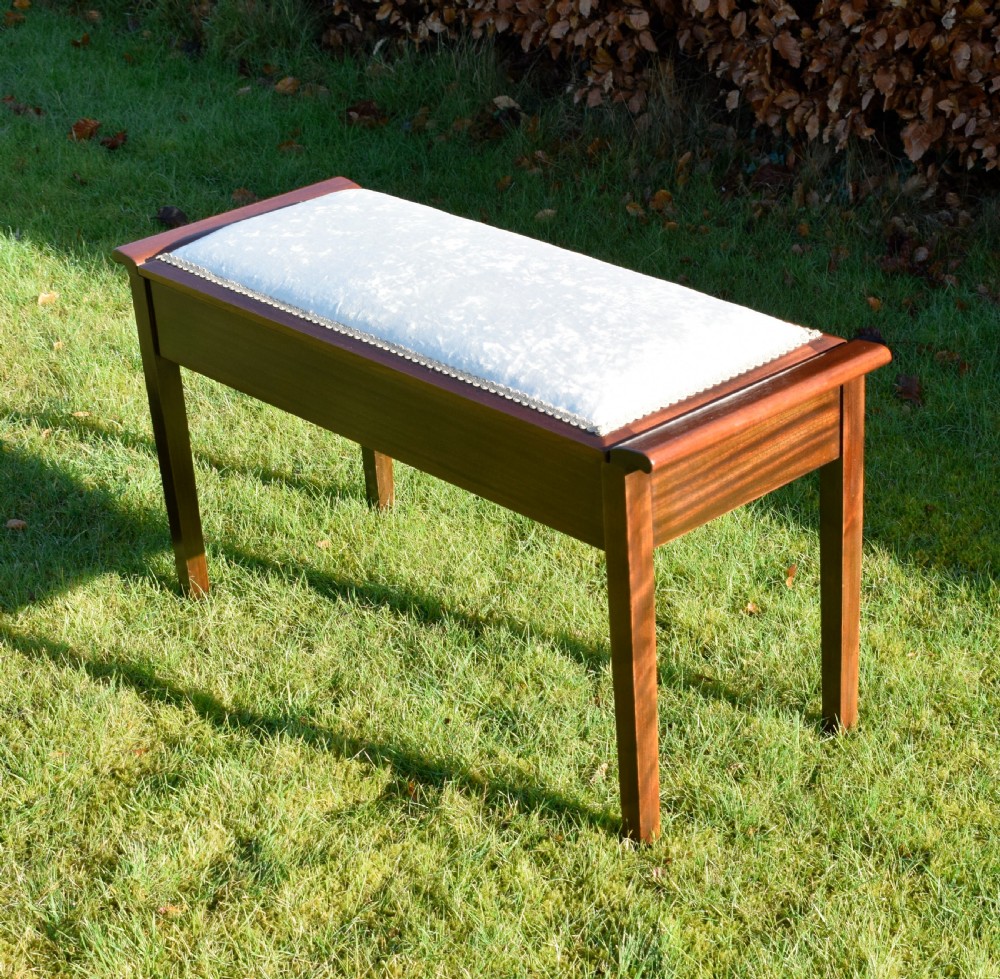 An Art Deco dark mahogany duet piano stool featuring a cushioned pale pink velvet seat with braided gimp trim and straight tapered legs. View V
