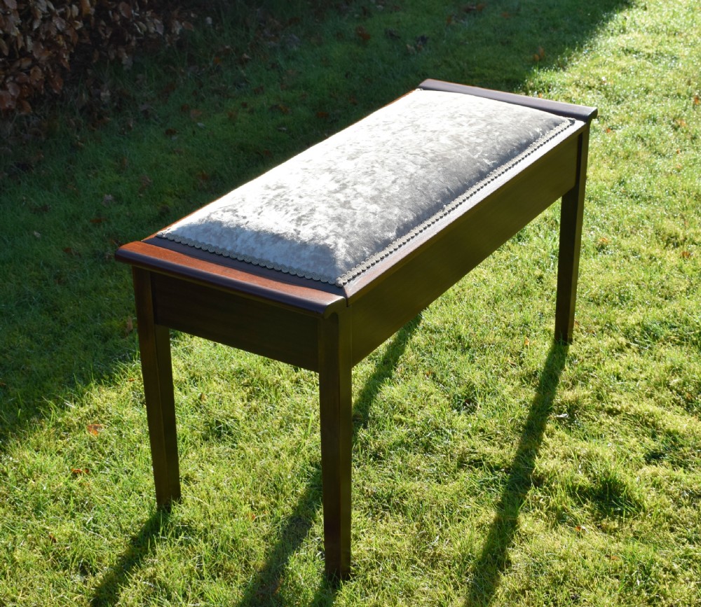 An Art Deco dark mahogany duet piano stool featuring a cushioned pale pink velvet seat with braided gimp trim and straight tapered legs. View VII