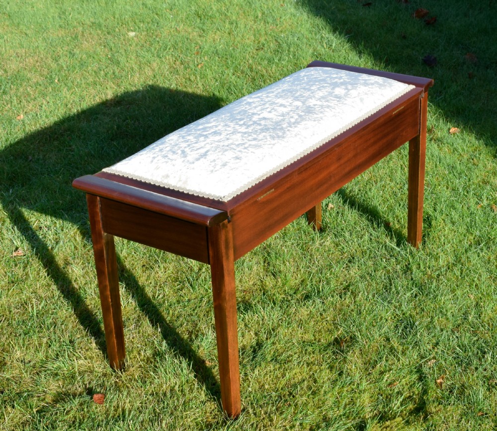 An Art Deco dark mahogany duet piano stool featuring a cushioned pale pink velvet seat with braided gimp trim and straight tapered legs. View X