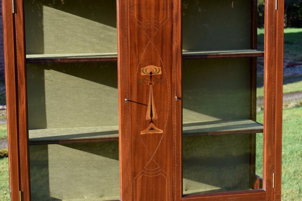 An early 20th-century mahogany Art Nouveau display cabinet featuring glazed doors, central inlaid botanical marquetry, and a fabric-lined interior on slender legs. View IV