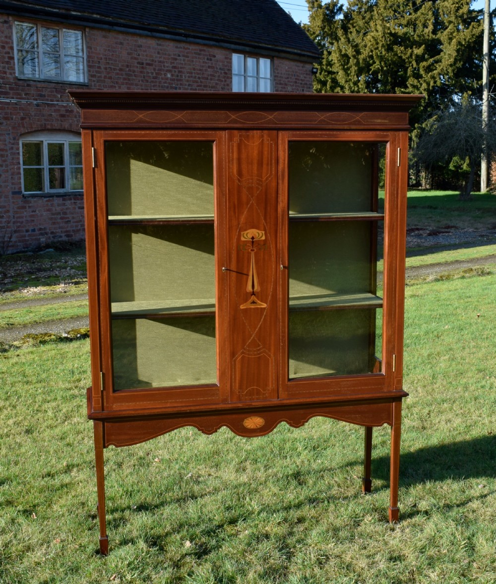 An early 20th-century mahogany Art Nouveau display cabinet featuring glazed doors, central inlaid botanical marquetry, and a fabric-lined interior on slender legs. View V