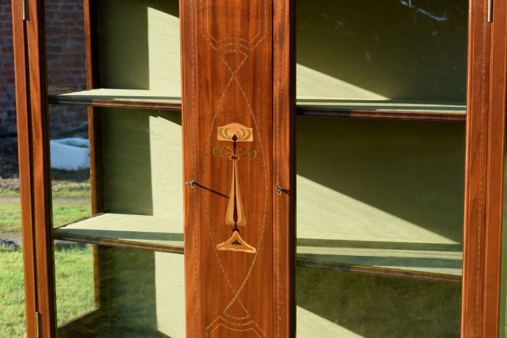 An early 20th-century mahogany Art Nouveau display cabinet featuring glazed doors, central inlaid botanical marquetry, and a fabric-lined interior on slender legs. View VII