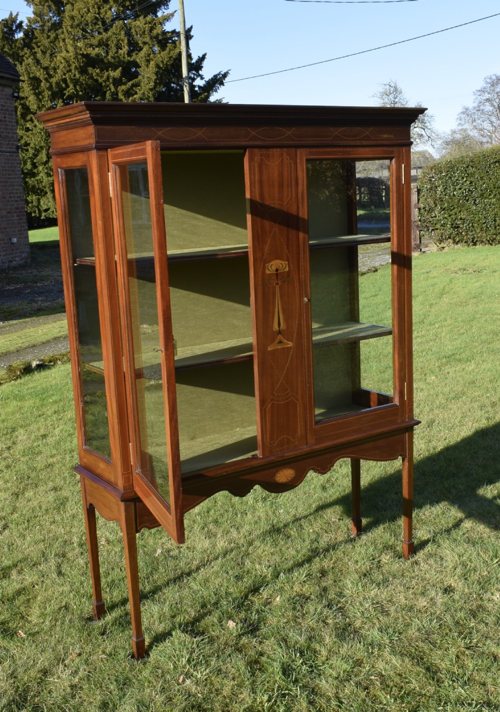 An early 20th-century mahogany Art Nouveau display cabinet featuring glazed doors, central inlaid botanical marquetry, and a fabric-lined interior on slender legs. View XVII