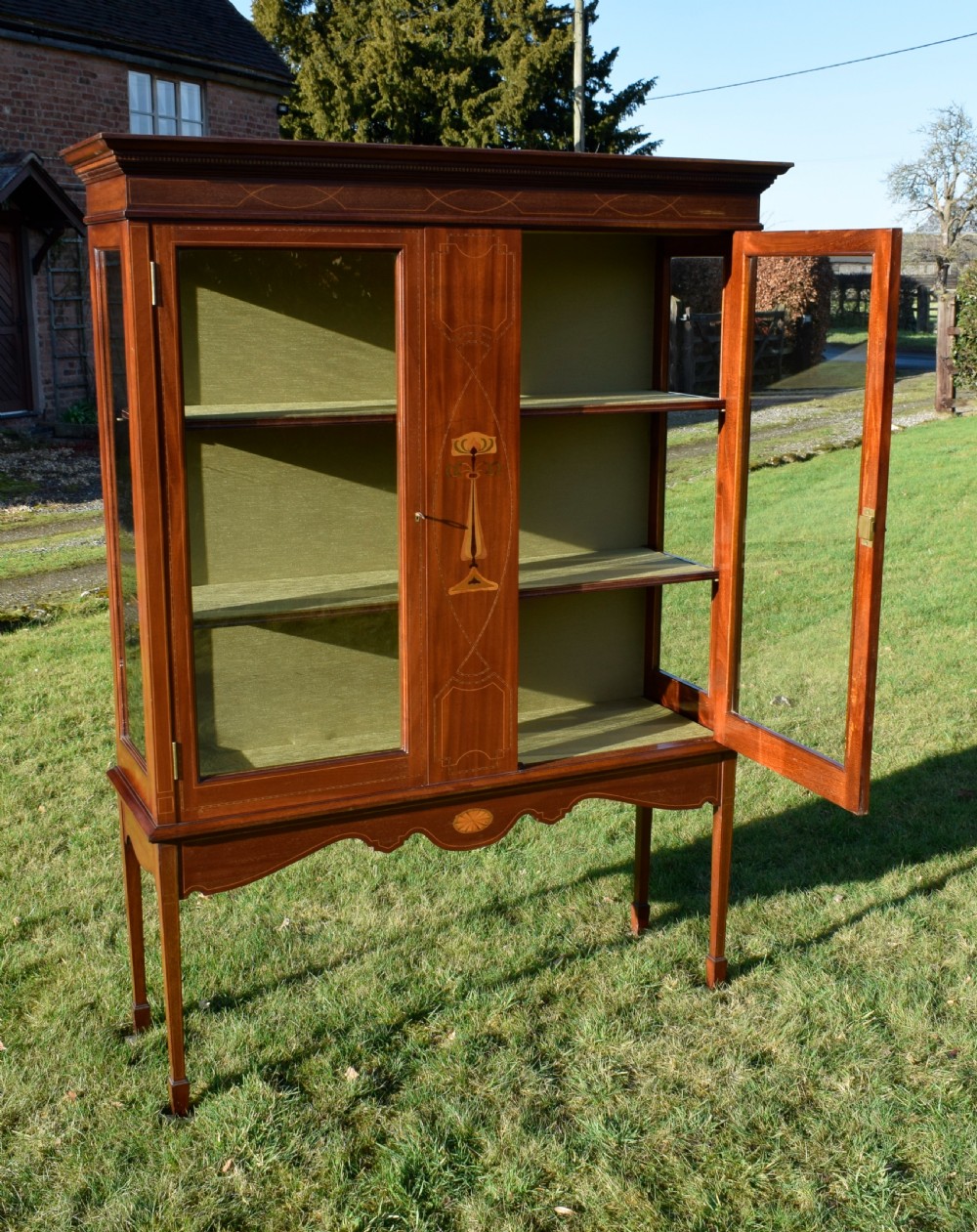 An early 20th-century mahogany Art Nouveau display cabinet featuring glazed doors, central inlaid botanical marquetry, and a fabric-lined interior on slender legs. View XVIII