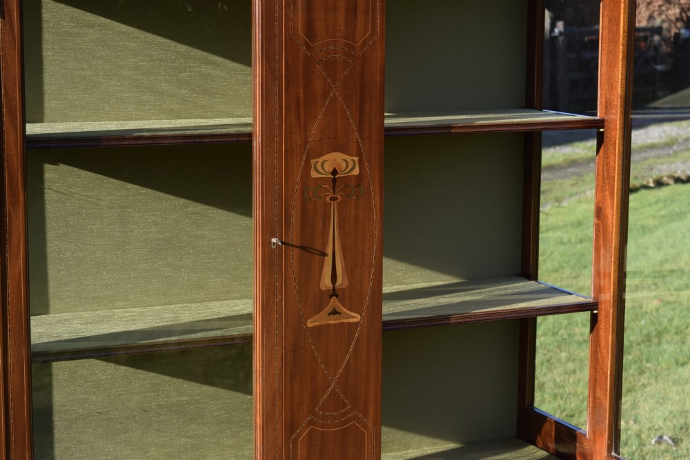 An early 20th-century mahogany Art Nouveau display cabinet featuring glazed doors, central inlaid botanical marquetry, and a fabric-lined interior on slender legs. View XIX