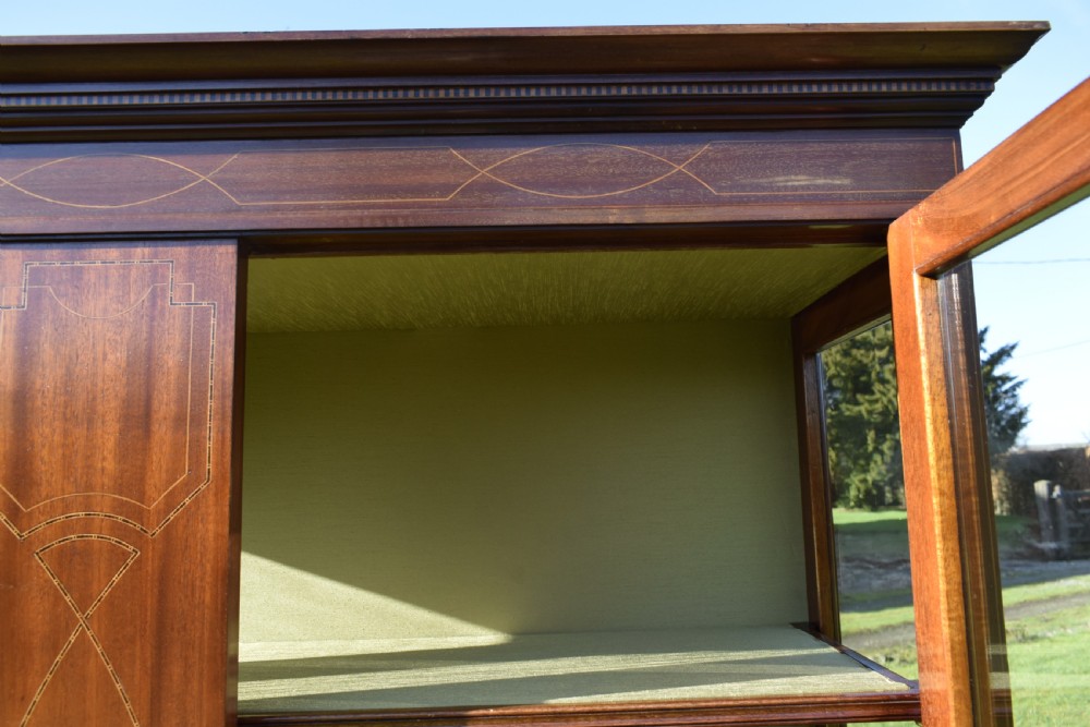 An early 20th-century mahogany Art Nouveau display cabinet featuring glazed doors, central inlaid botanical marquetry, and a fabric-lined interior on slender legs. View XX