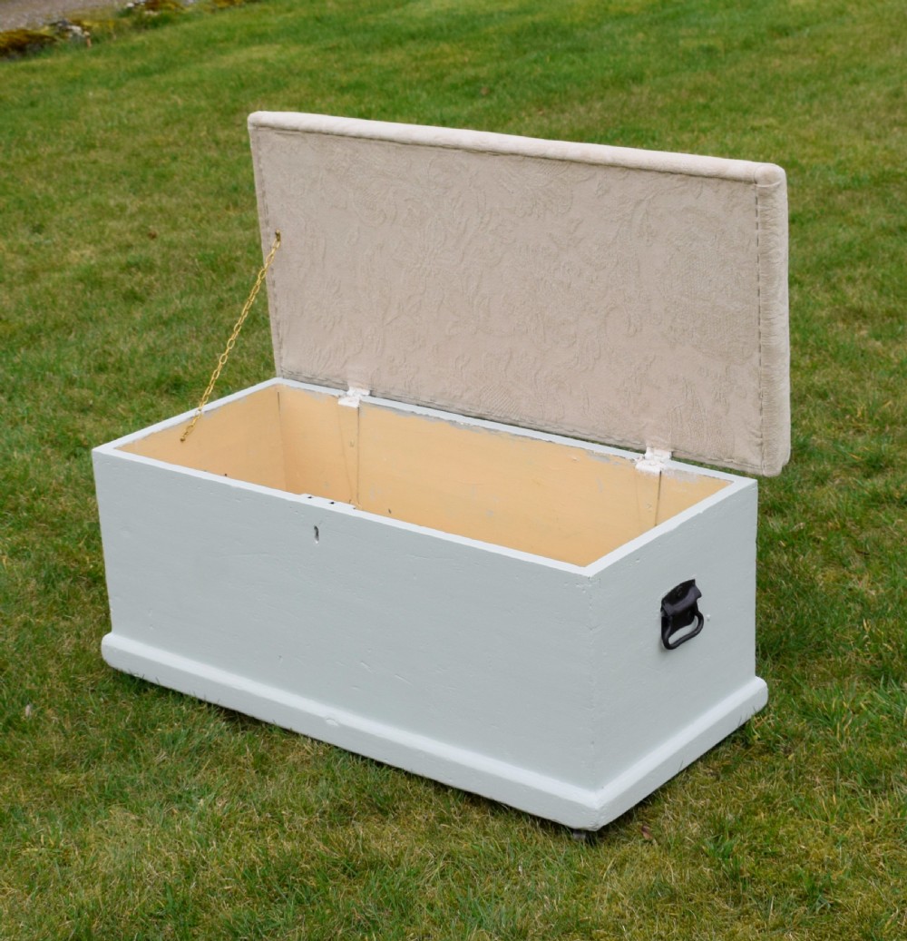 A Victorian painted pine blanket box featuring a cream upholstered cushioned top and iron drop side handles. View X
