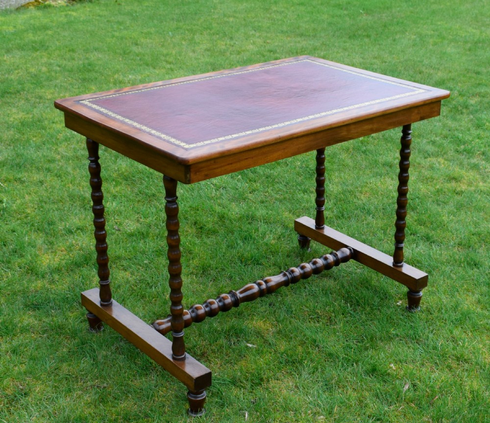 A Victorian mahogany writing table with turned legs, a stretcher base, and an inset red leather top framed with gold leaf tooling.