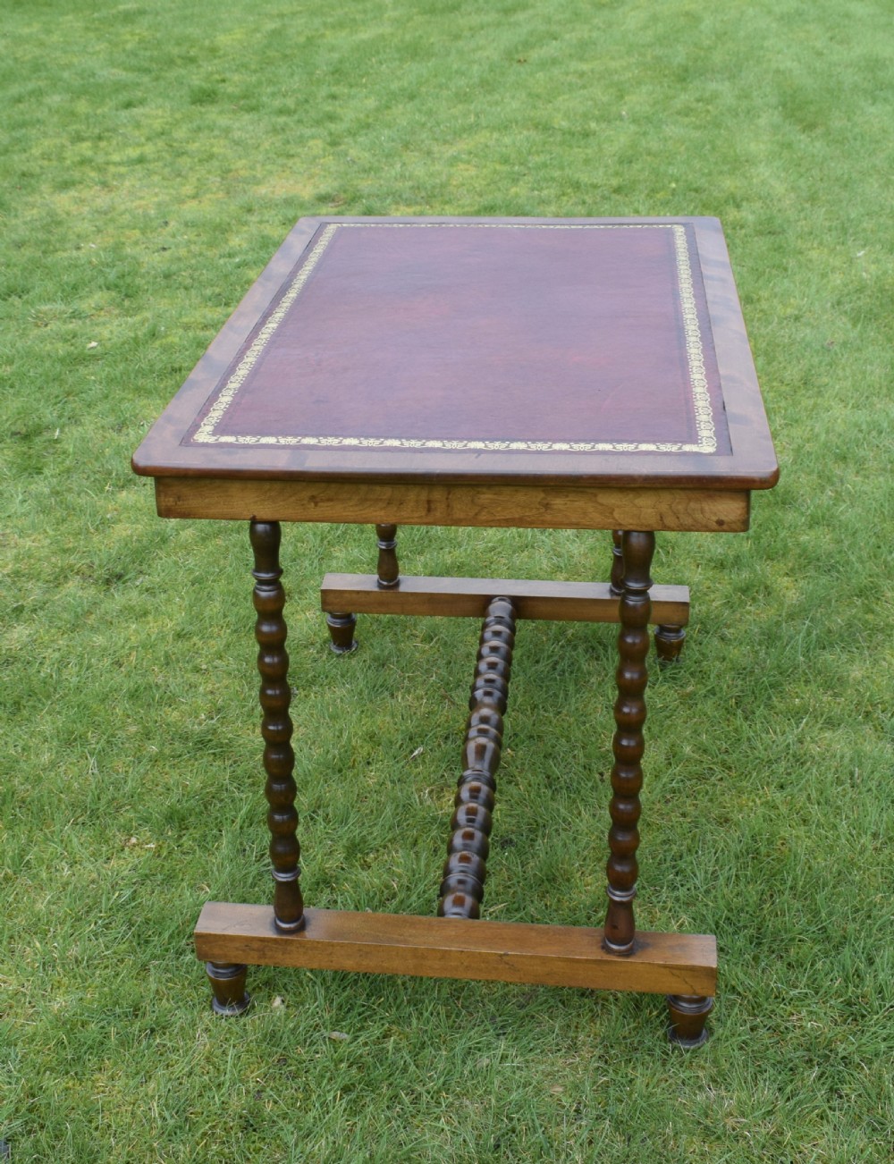 A Victorian mahogany writing table with turned legs, a stretcher base, and an inset red leather top framed with gold leaf tooling. View II