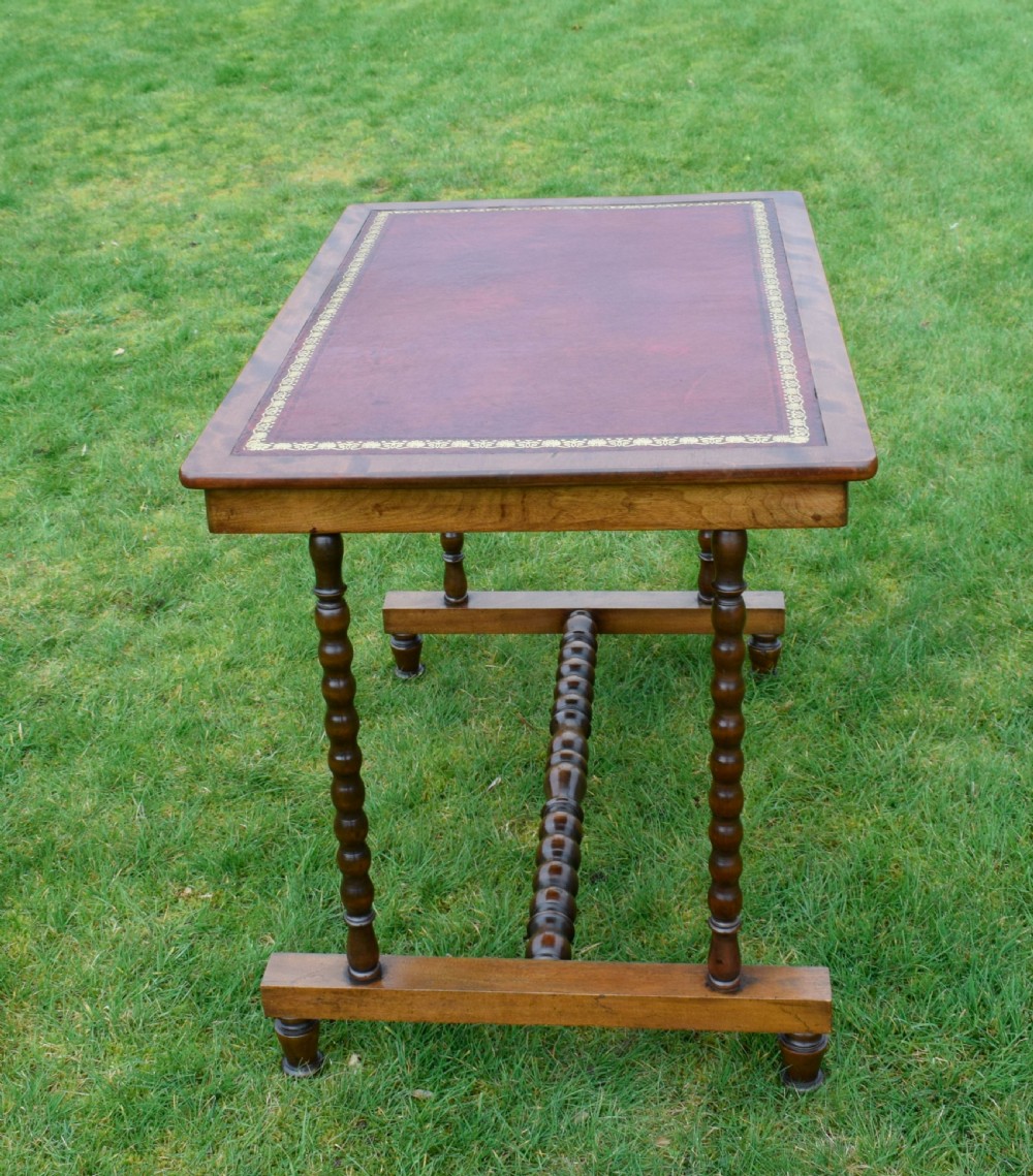 A Victorian mahogany writing table with turned legs, a stretcher base, and an inset red leather top framed with gold leaf tooling. View III
