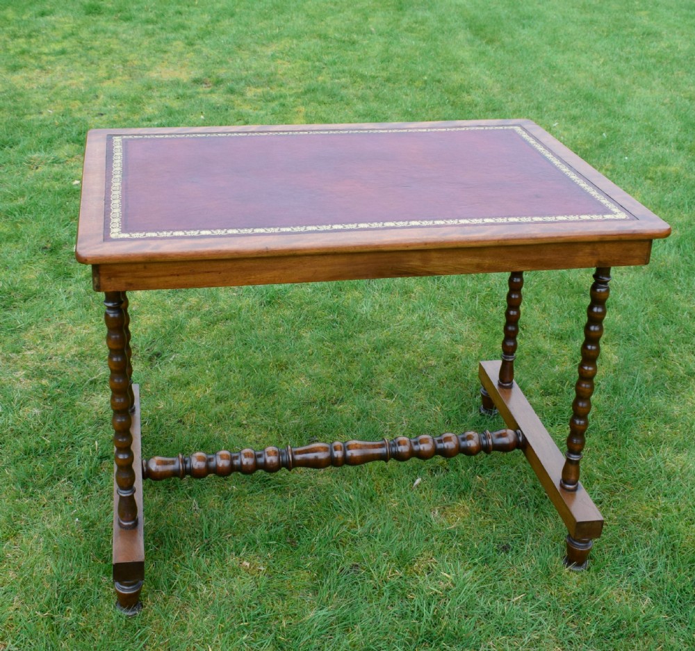 A Victorian mahogany writing table with turned legs, a stretcher base, and an inset red leather top framed with gold leaf tooling. View IV