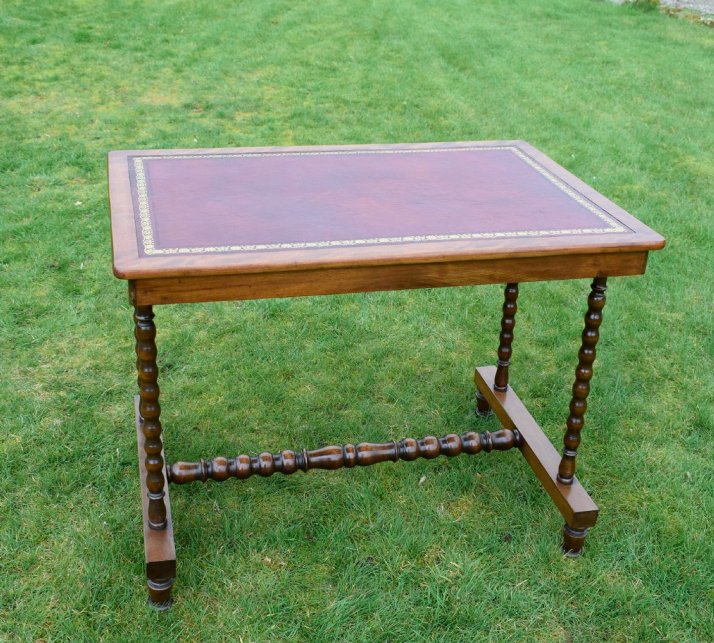 A Victorian mahogany writing table with turned legs, a stretcher base, and an inset red leather top framed with gold leaf tooling. View V