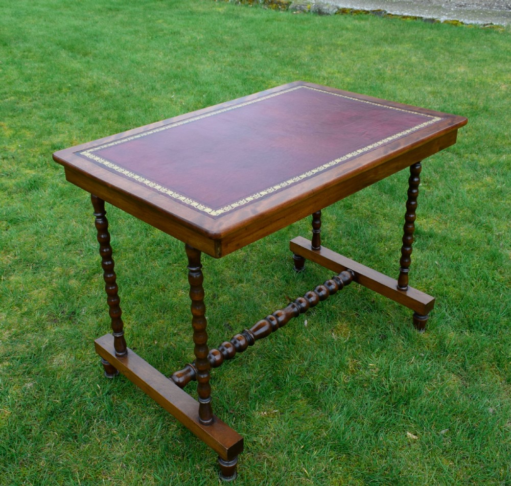 A Victorian mahogany writing table with turned legs, a stretcher base, and an inset red leather top framed with gold leaf tooling. View VI