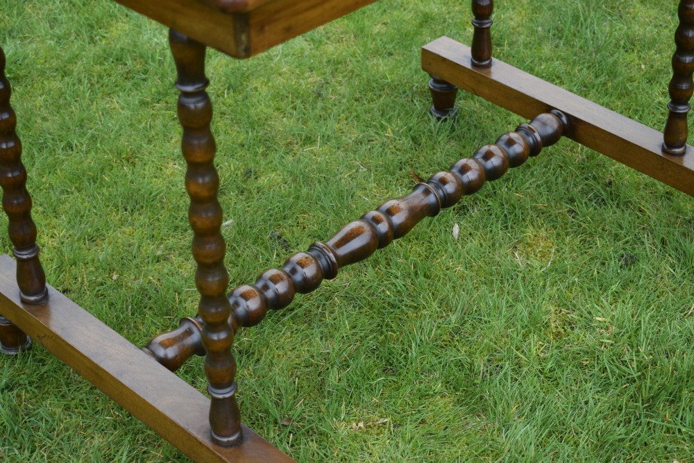 A Victorian mahogany writing table with turned legs, a stretcher base, and an inset red leather top framed with gold leaf tooling. View VII