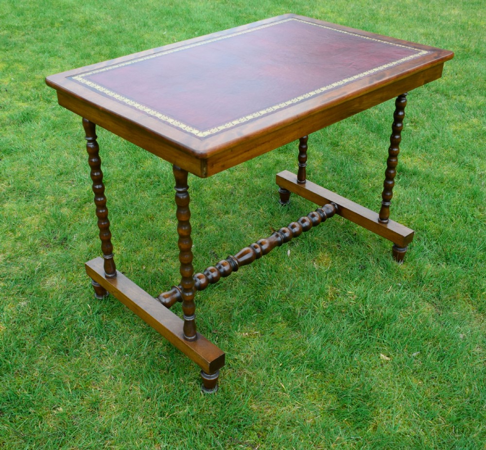 A Victorian mahogany writing table with turned legs, a stretcher base, and an inset red leather top framed with gold leaf tooling. View VIII