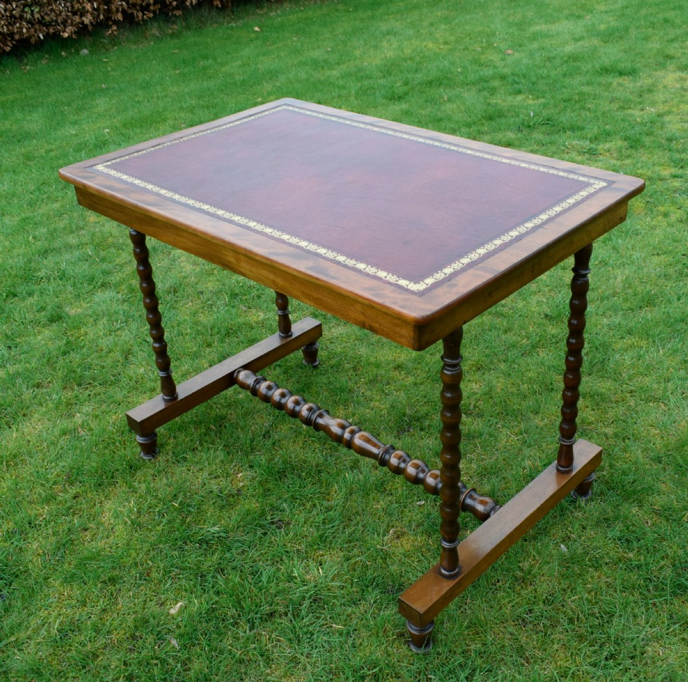 A Victorian mahogany writing table with turned legs, a stretcher base, and an inset red leather top framed with gold leaf tooling. View IX