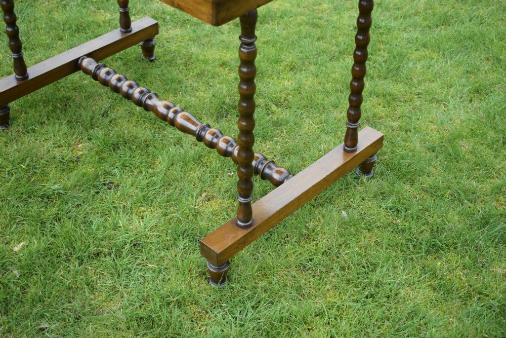 A Victorian mahogany writing table with turned legs, a stretcher base, and an inset red leather top framed with gold leaf tooling. View X