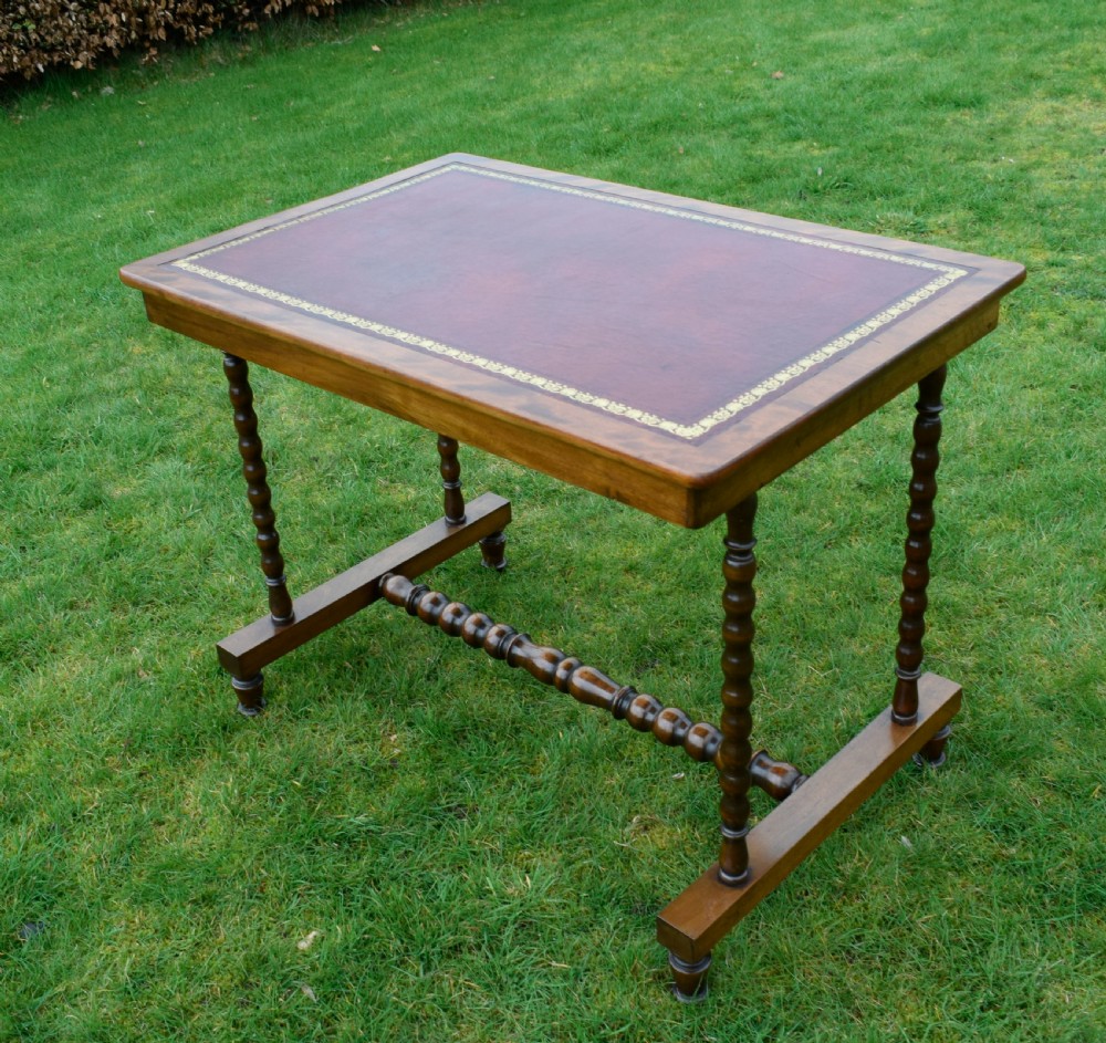 A Victorian mahogany writing table with turned legs, a stretcher base, and an inset red leather top framed with gold leaf tooling. View XI