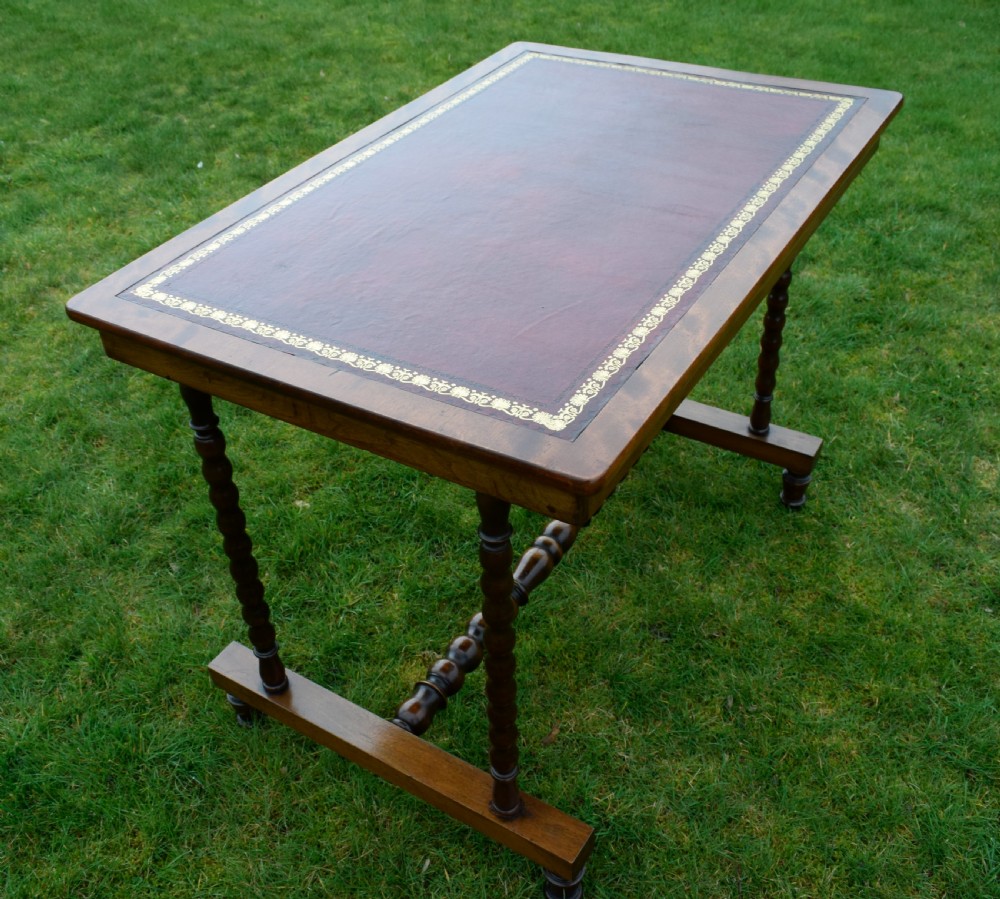 A Victorian mahogany writing table with turned legs, a stretcher base, and an inset red leather top framed with gold leaf tooling. View XII