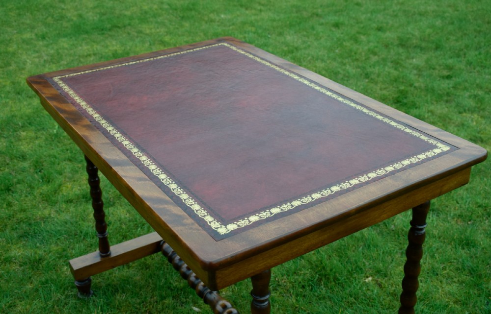 A Victorian mahogany writing table with turned legs, a stretcher base, and an inset red leather top framed with gold leaf tooling. View XVIII