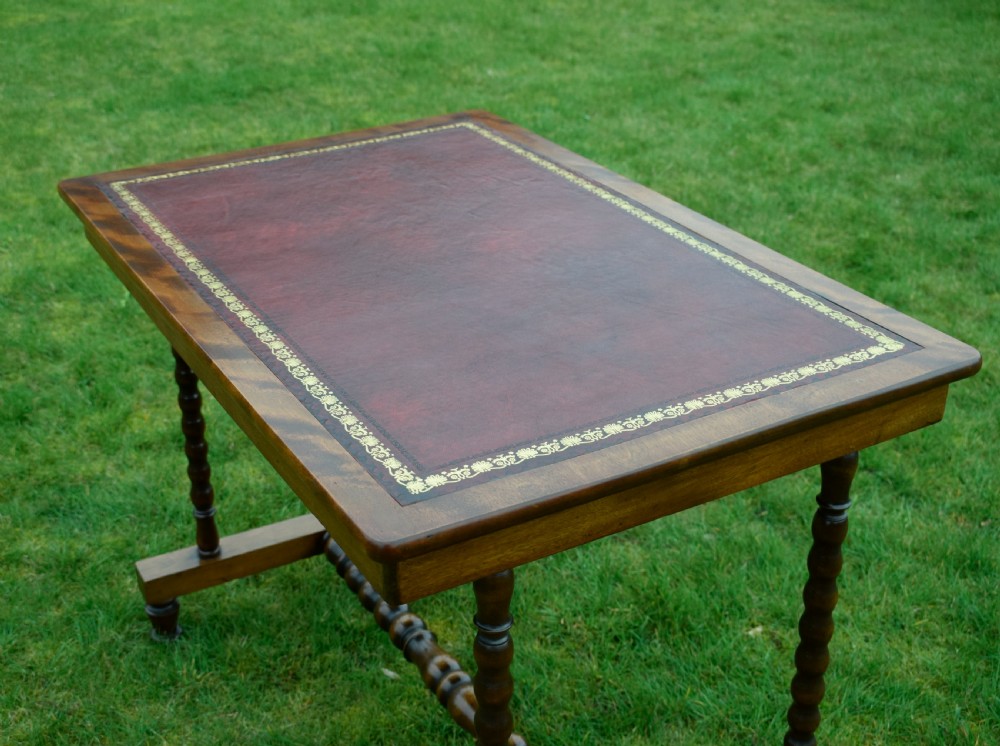 A Victorian mahogany writing table with turned legs, a stretcher base, and an inset red leather top framed with gold leaf tooling. View XIX