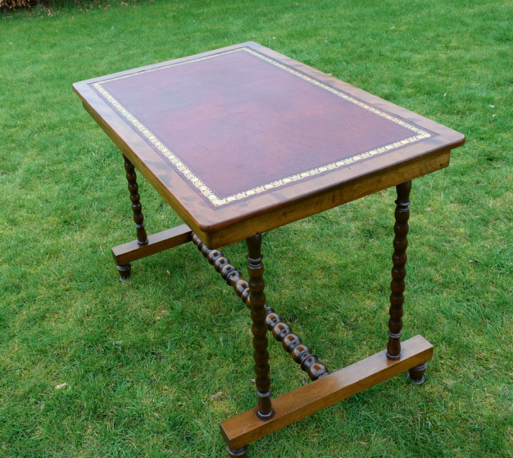 A Victorian mahogany writing table with turned legs, a stretcher base, and an inset red leather top framed with gold leaf tooling. View XXI