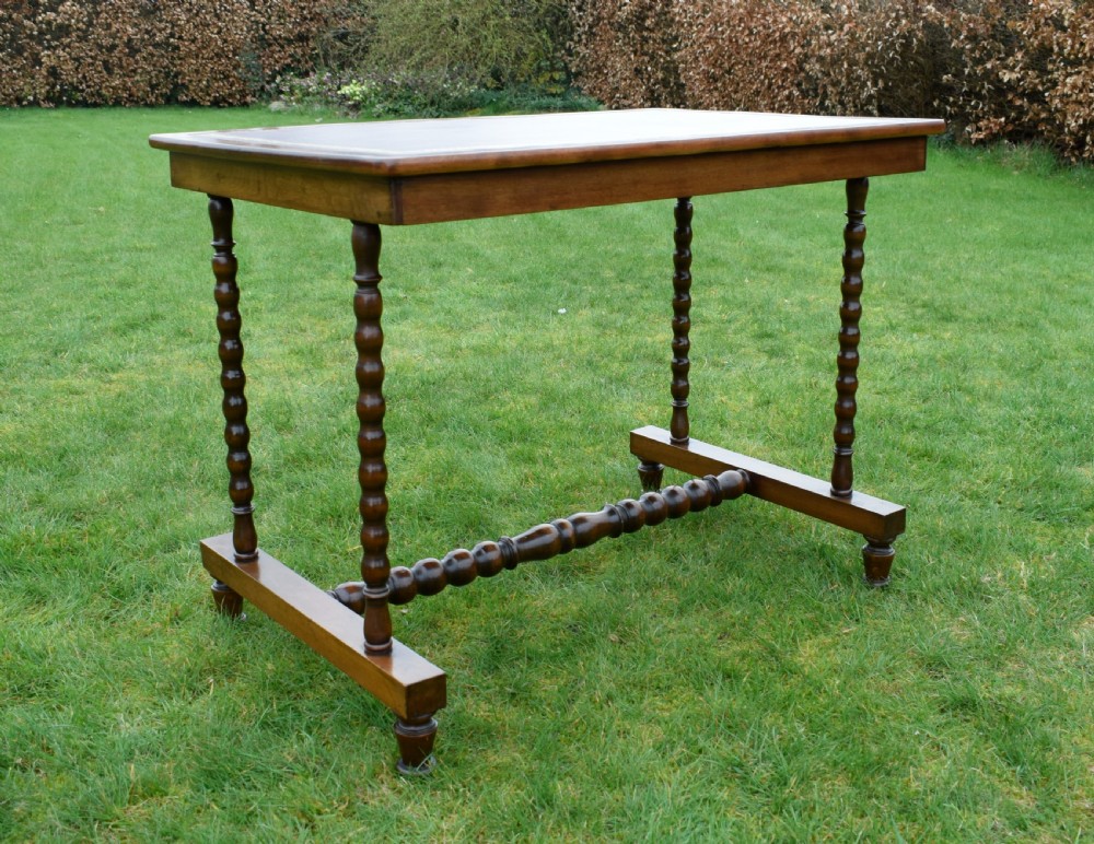 A Victorian mahogany writing table with turned legs, a stretcher base, and an inset red leather top framed with gold leaf tooling. View XXII
