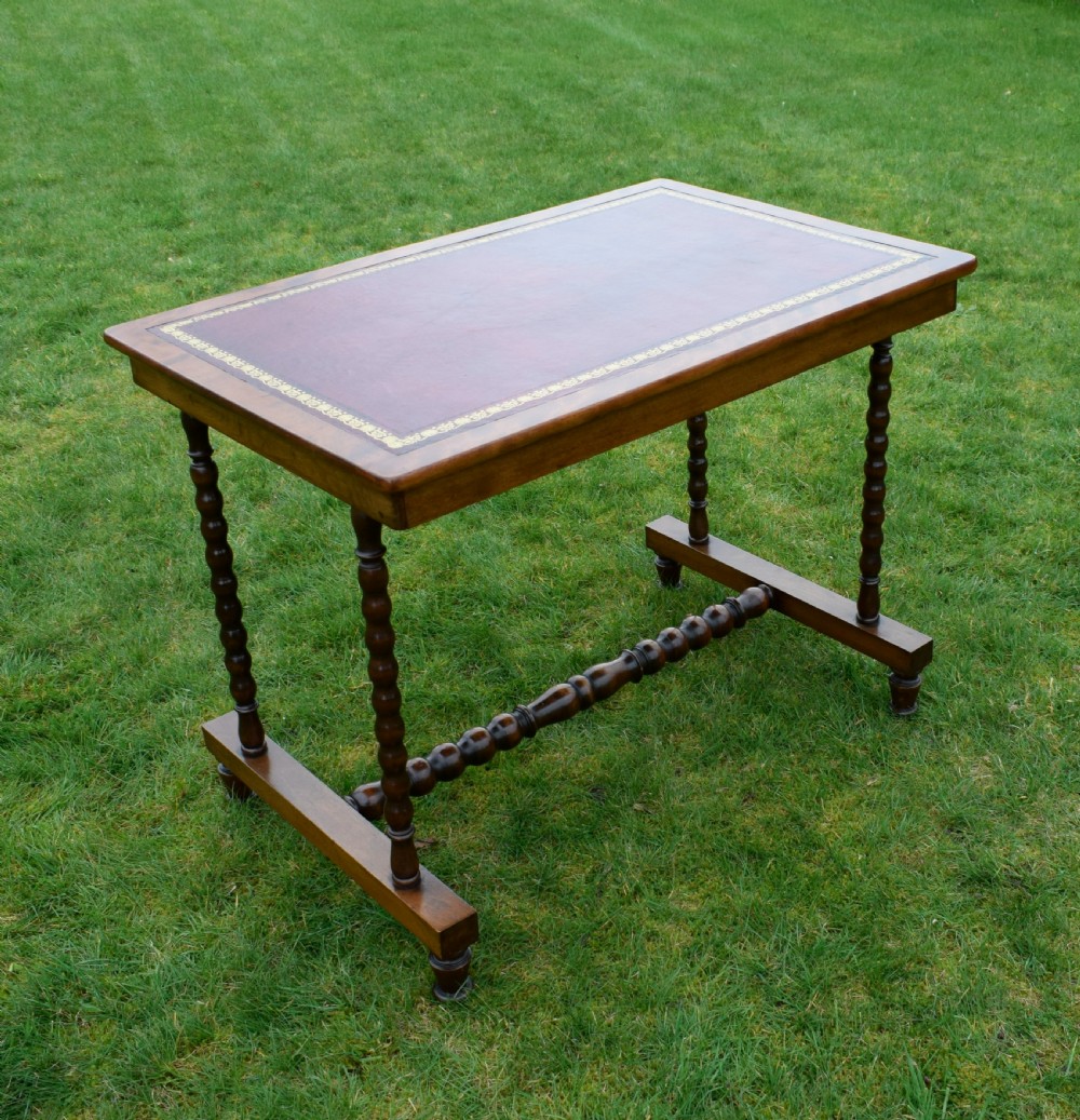 A Victorian mahogany writing table with turned legs, a stretcher base, and an inset red leather top framed with gold leaf tooling. View XXIII