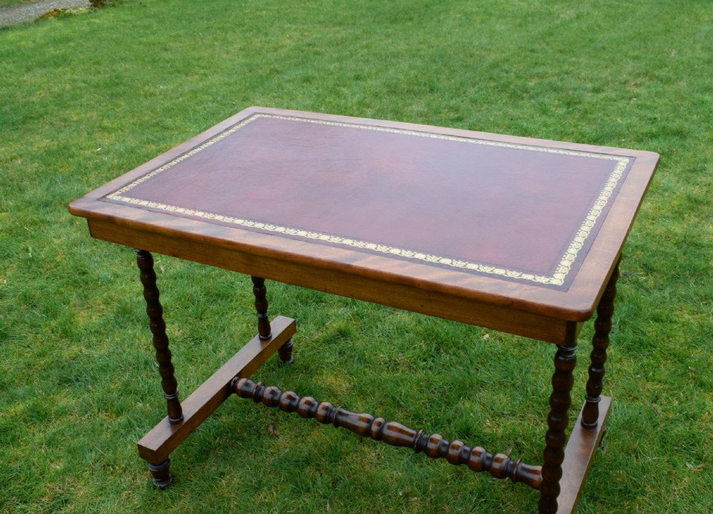 A Victorian mahogany writing table with turned legs, a stretcher base, and an inset red leather top framed with gold leaf tooling. View XXIV