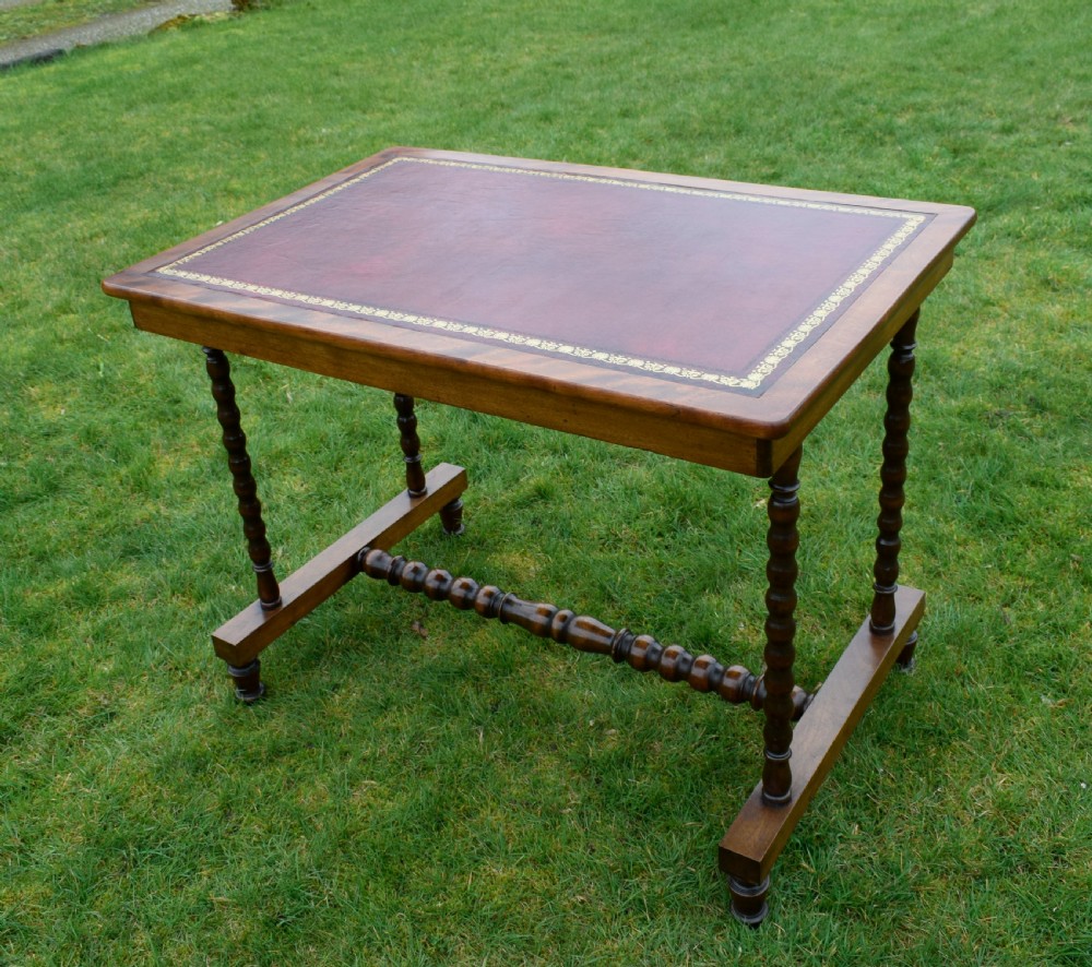 A Victorian mahogany writing table with turned legs, a stretcher base, and an inset red leather top framed with gold leaf tooling. View XXV