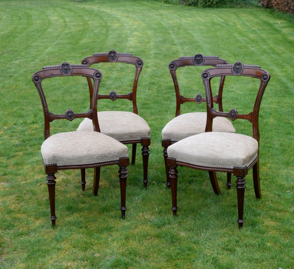 Set of four Victorian walnut dining chairs with carved open backs, turned front legs, and beige fabric upholstered seats.