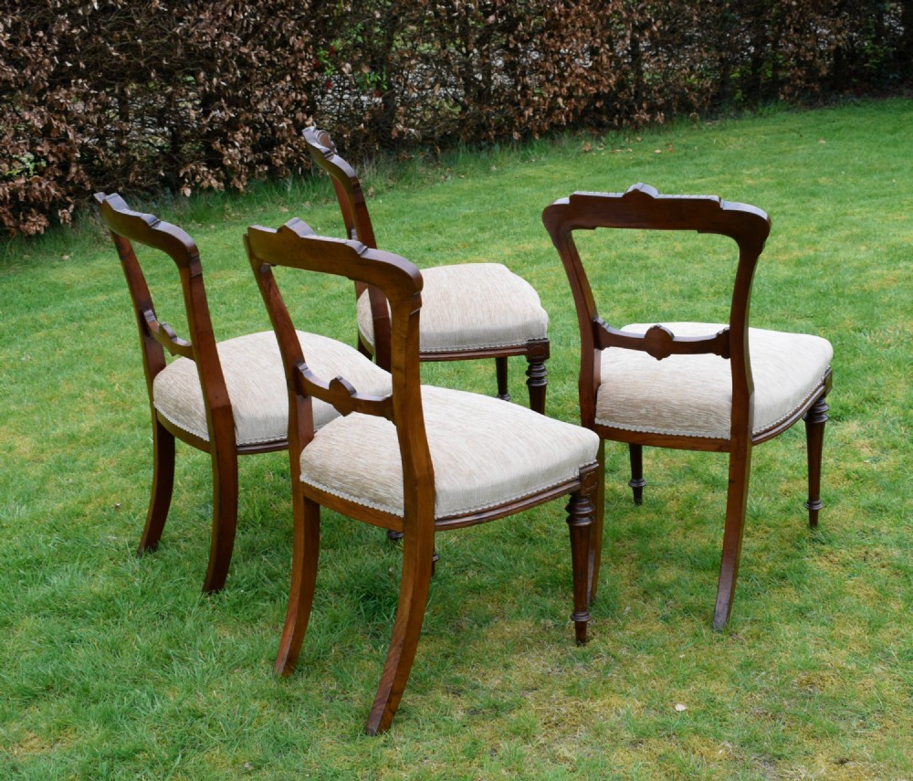 Set of four Victorian walnut dining chairs with carved open backs, turned front legs, and beige fabric upholstered seats. View VI