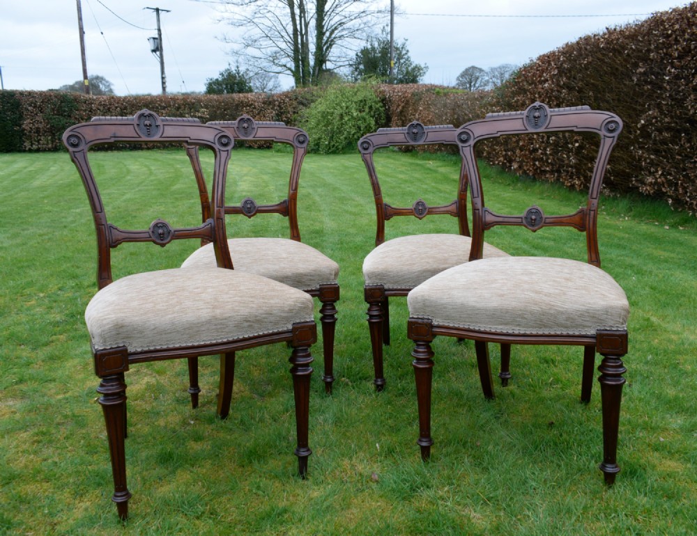Set of four Victorian walnut dining chairs with carved open backs, turned front legs, and beige fabric upholstered seats. View X