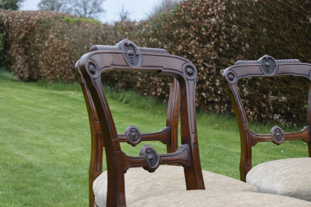 Set of four Victorian walnut dining chairs with carved open backs, turned front legs, and beige fabric upholstered seats. View XV