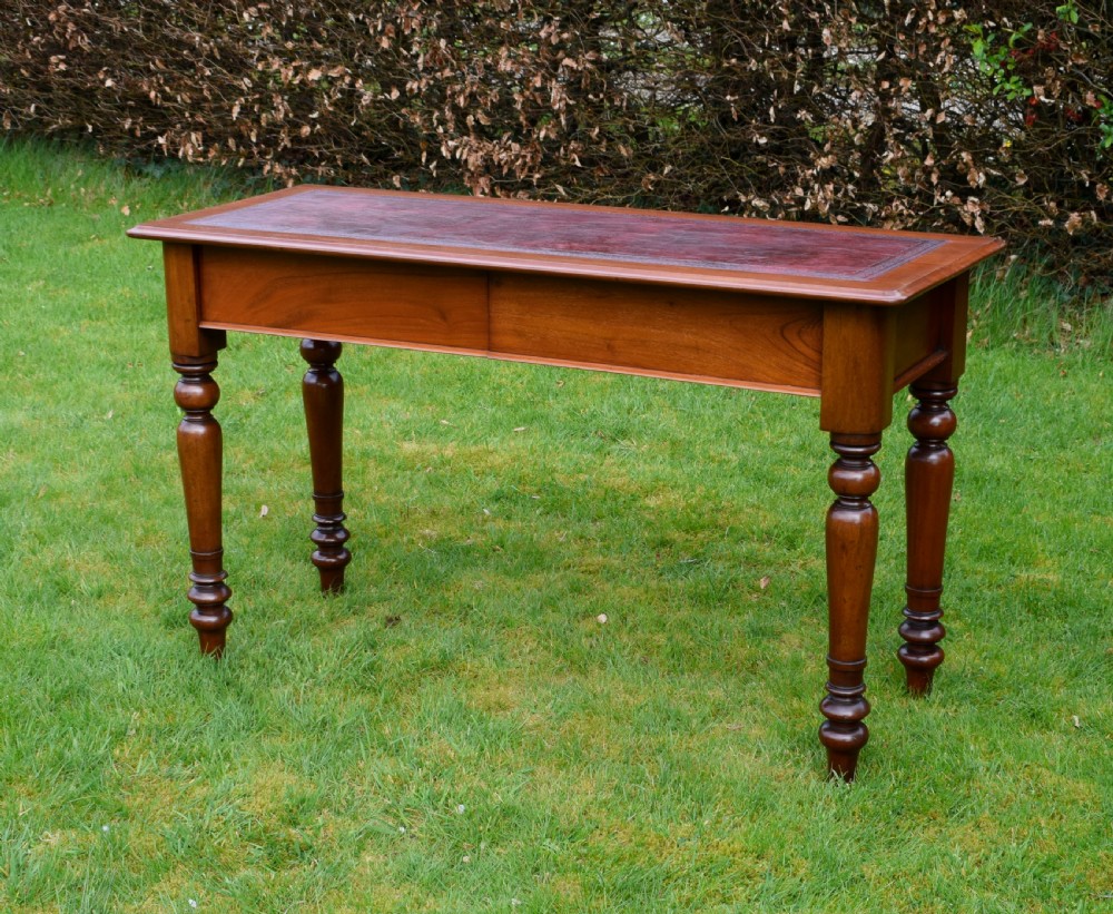A rectangular Victorian mahogany writing desk featuring a burgundy leather inset top, two frieze drawers, and four turned wooden legs.