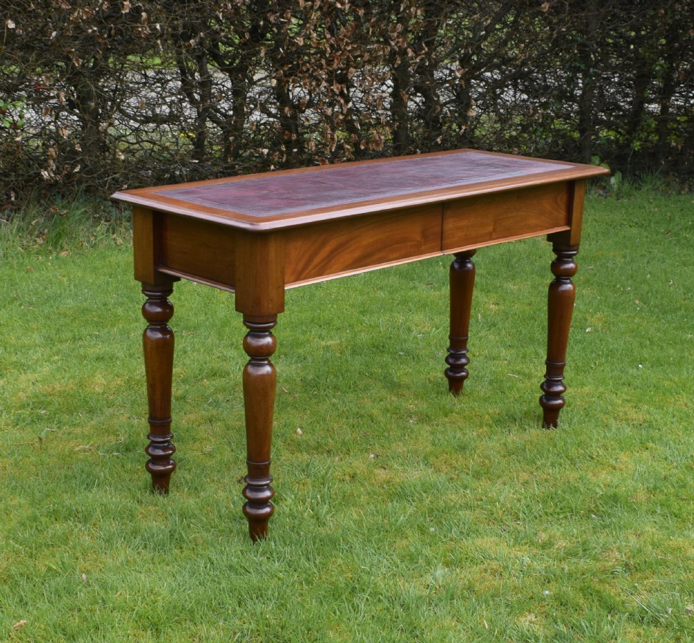 A rectangular Victorian mahogany writing desk featuring a burgundy leather inset top, two frieze drawers, and four turned wooden legs. View II