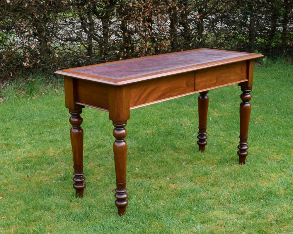 A rectangular Victorian mahogany writing desk featuring a burgundy leather inset top, two frieze drawers, and four turned wooden legs. View III