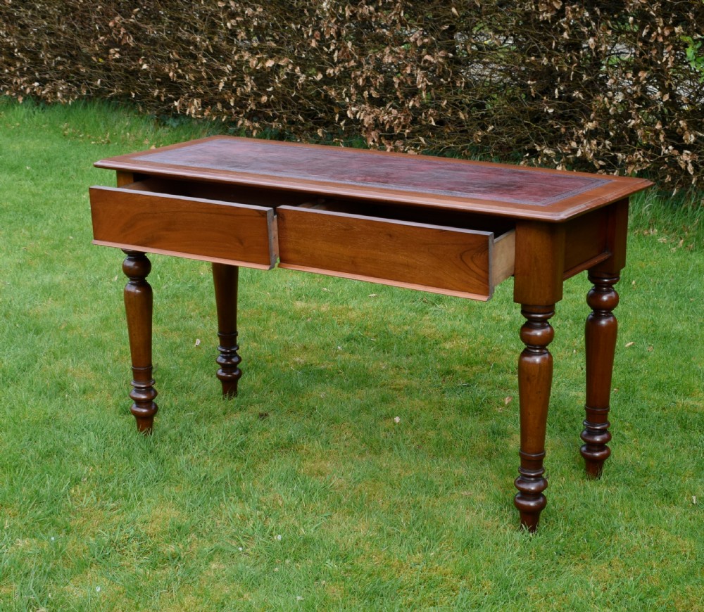 A rectangular Victorian mahogany writing desk featuring a burgundy leather inset top, two frieze drawers, and four turned wooden legs. View V