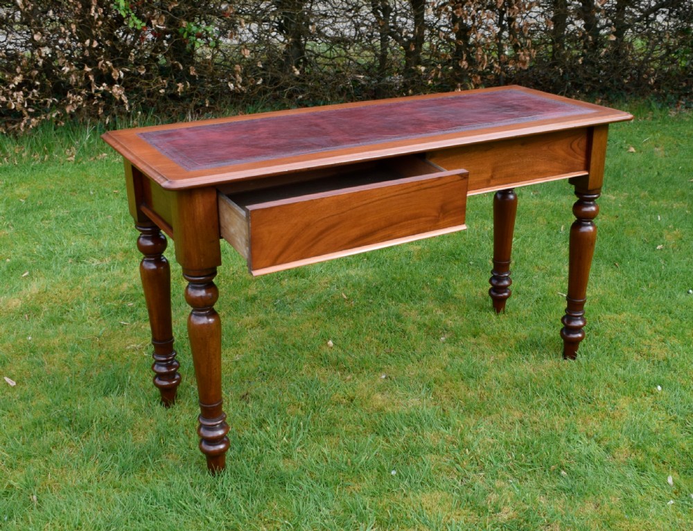 A rectangular Victorian mahogany writing desk featuring a burgundy leather inset top, two frieze drawers, and four turned wooden legs. View VI