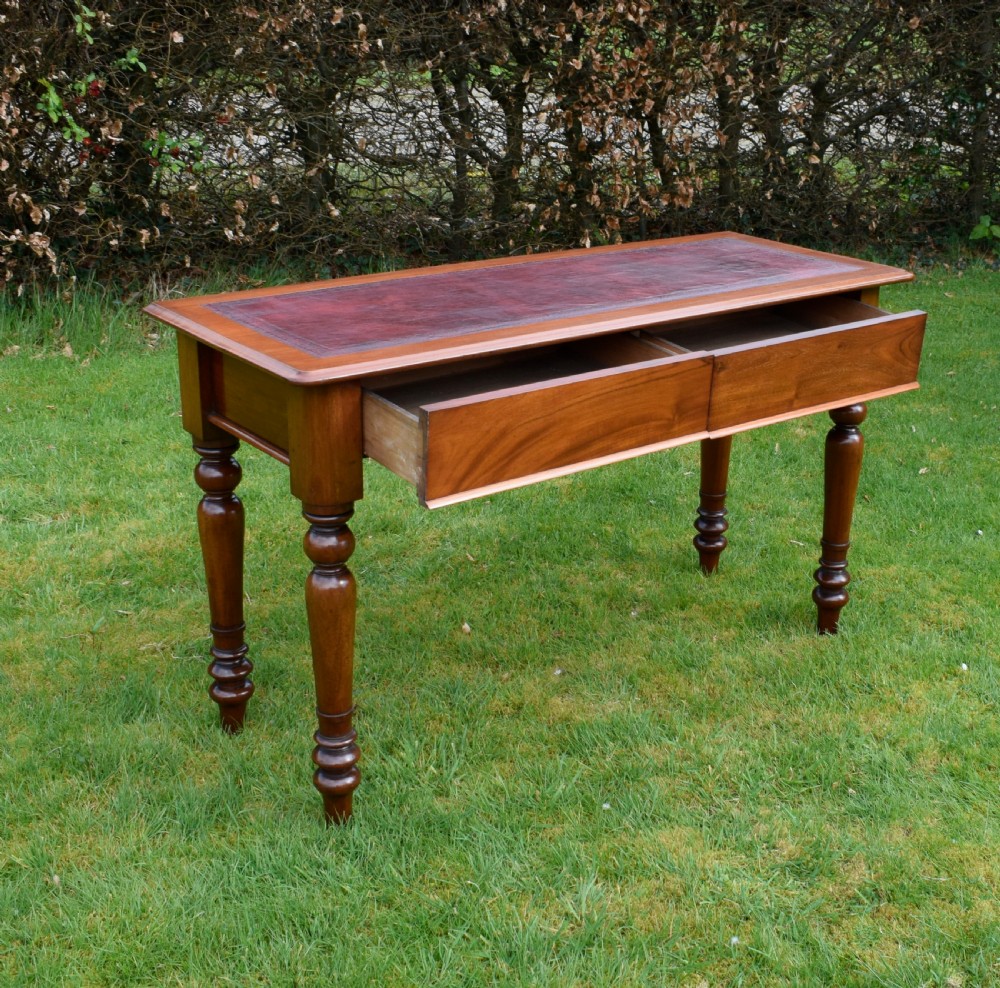 A rectangular Victorian mahogany writing desk featuring a burgundy leather inset top, two frieze drawers, and four turned wooden legs. View VII