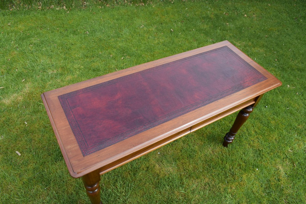 A rectangular Victorian mahogany writing desk featuring a burgundy leather inset top, two frieze drawers, and four turned wooden legs. View IX