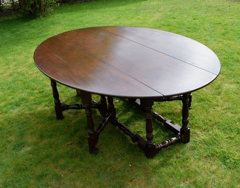 An early twentieth-century dark oak oval wake dining table with two drop-leaf flaps, turned legs, and base stretchers.