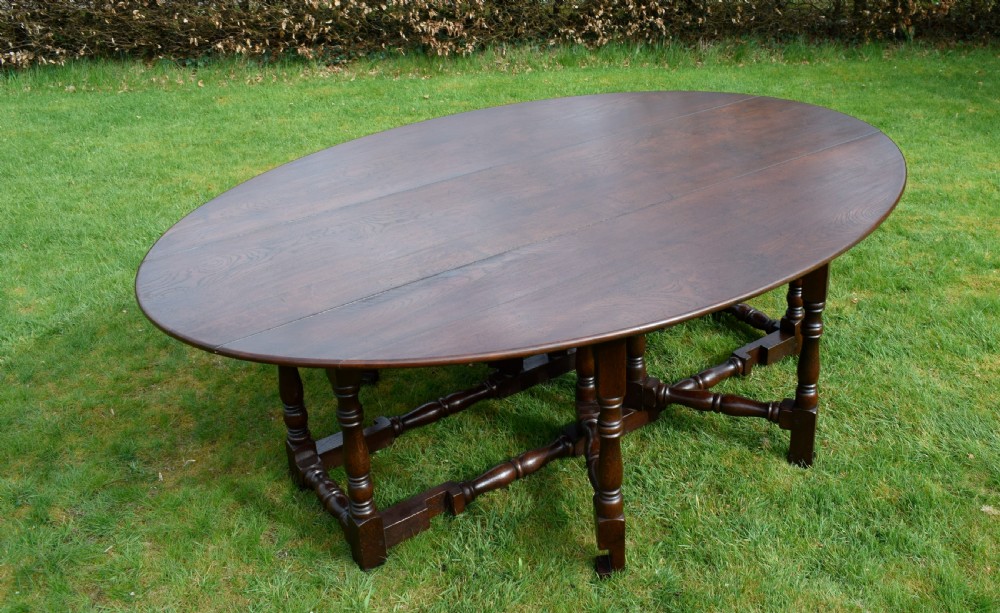 An early twentieth-century dark oak oval wake dining table with two drop-leaf flaps, turned legs, and base stretchers. View II
