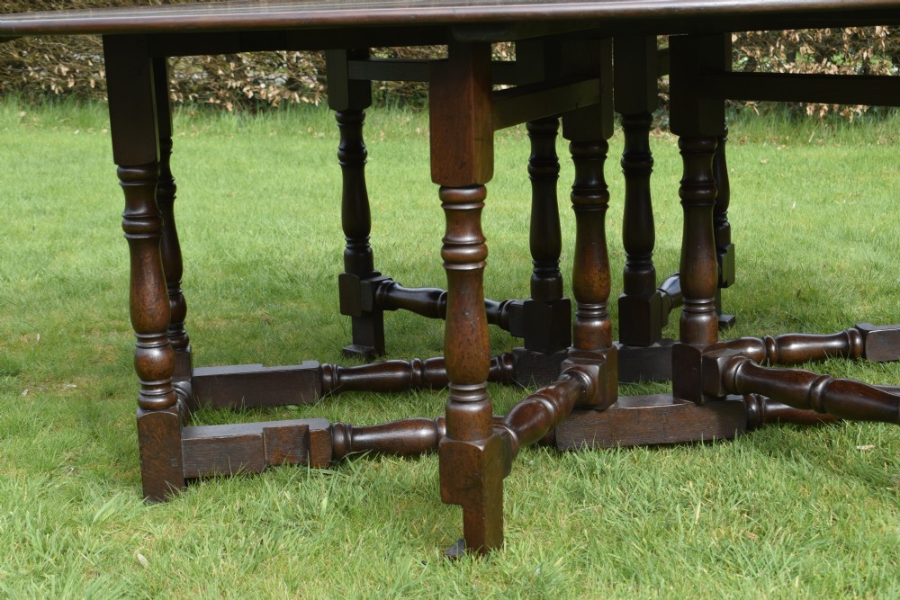 An early twentieth-century dark oak oval wake dining table with two drop-leaf flaps, turned legs, and base stretchers. View IV