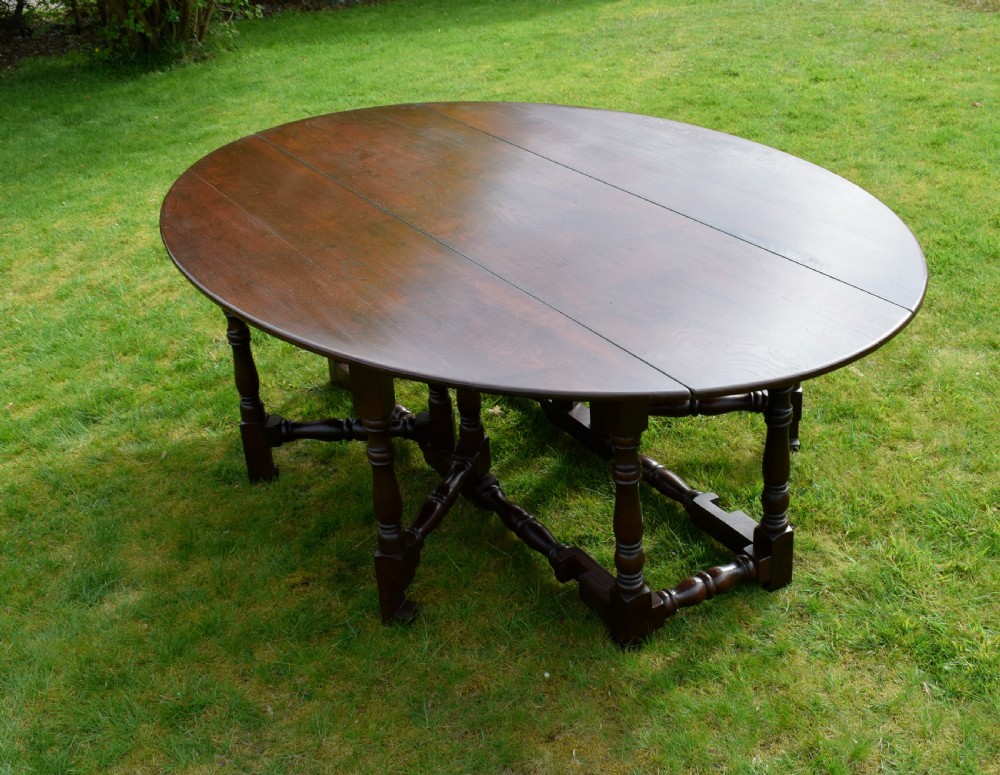 An early twentieth-century dark oak oval wake dining table with two drop-leaf flaps, turned legs, and base stretchers. View VI