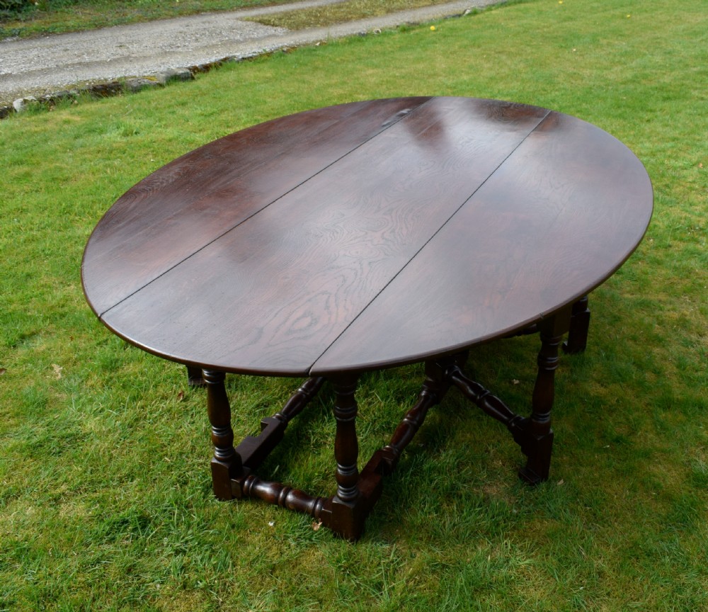 An early twentieth-century dark oak oval wake dining table with two drop-leaf flaps, turned legs, and base stretchers. View VII